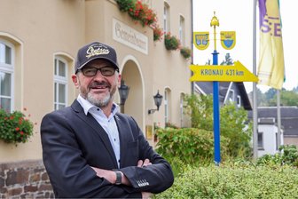 Dorfbürgermeister aus dem Erzgebirge: Warum ich die DDR nicht zurückwill - Lutz Rosenlöcher vor dem Rathaus. Der Wegweiser rechts gibt die Entfernung in die Partnergemeinde in Baden-Württemberg an.